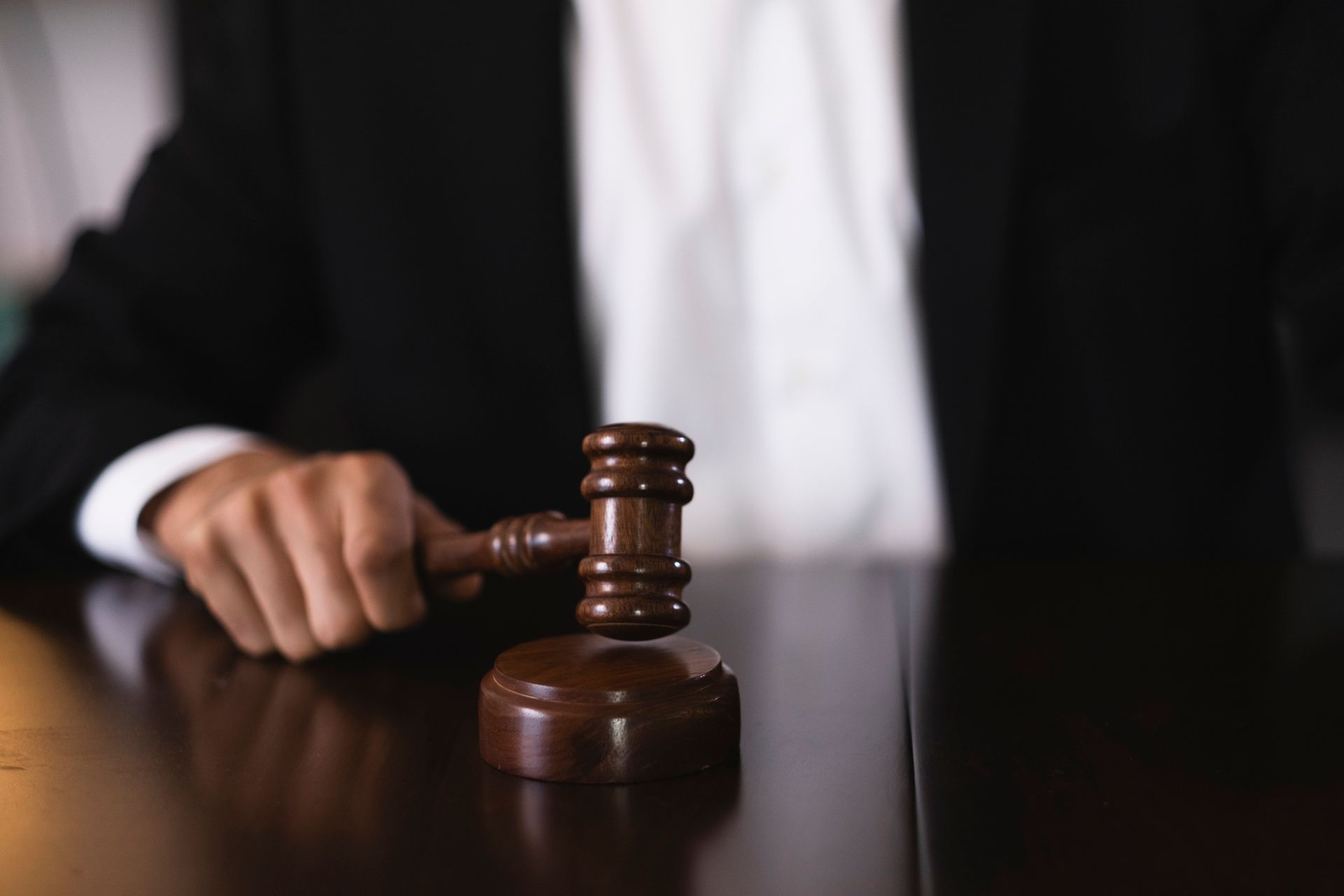 Close-up of a hand holding a wooden gavel on a desk in a courtroom setting. Close-up of a hand holding a wooden gavel on a desk in a courtroom setting.