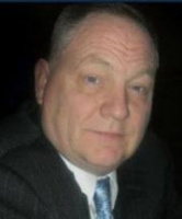 Man in suit and tie, looking to the side. Dark background.