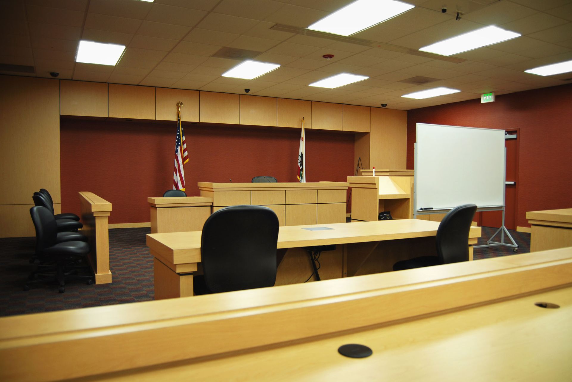Empty courtroom with wooden furniture, US and state flags, and a whiteboard.