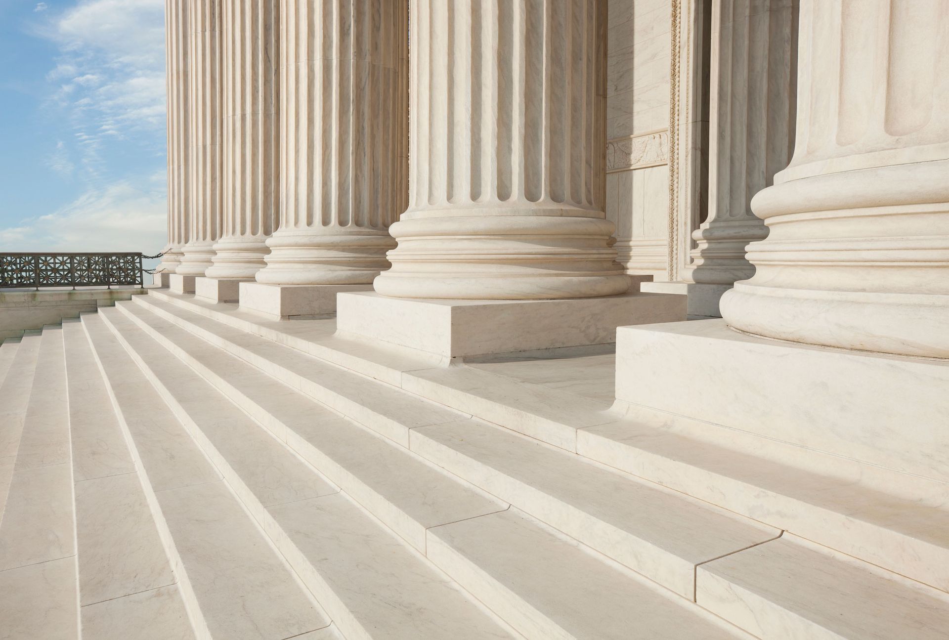 Exterior view of white steps and columns of a government building against a blue sky.