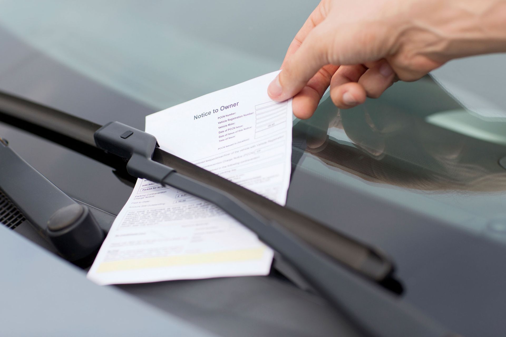 Hand placing a parking ticket under a windshield wiper on a car.