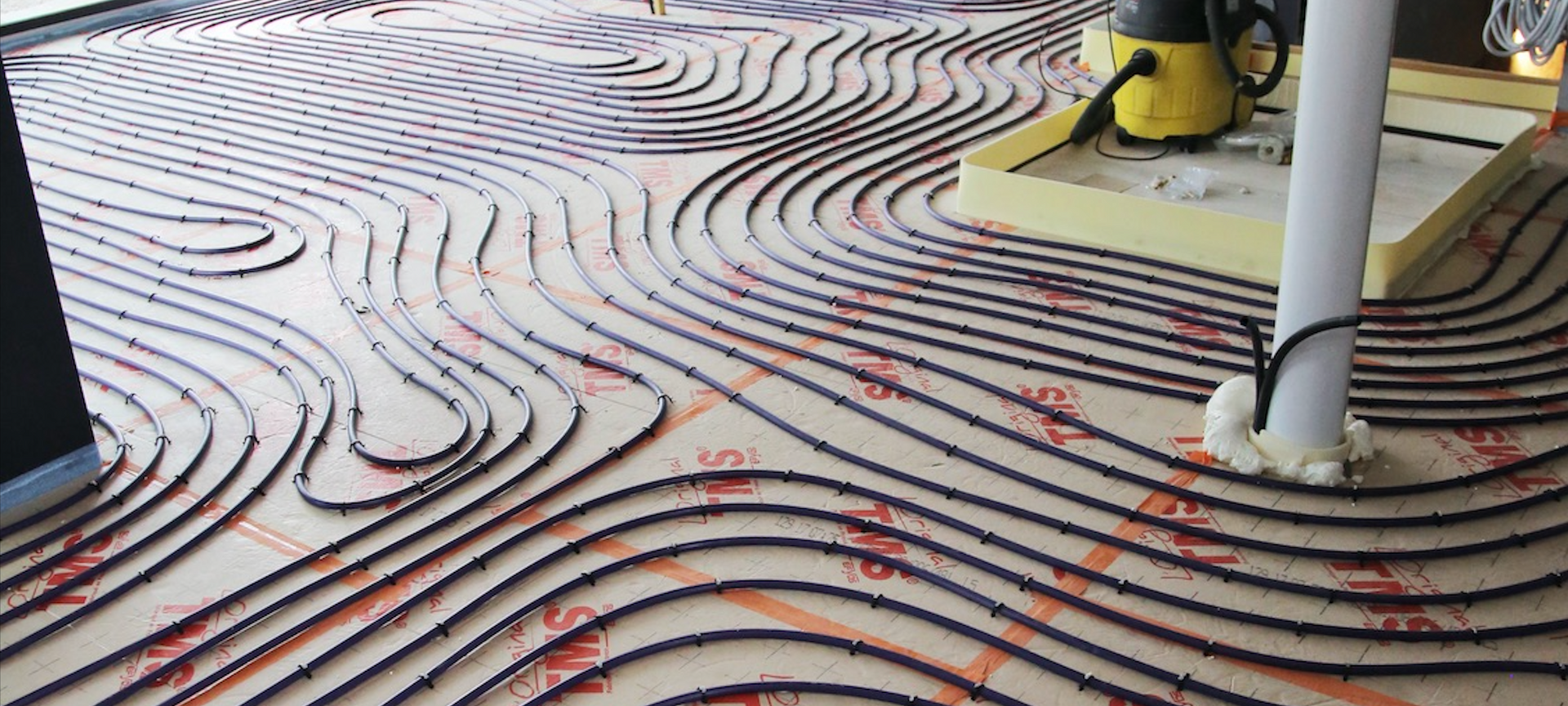 Un gros plan d'un système de chauffage au sol avec un aspirateur en arrière-plan.