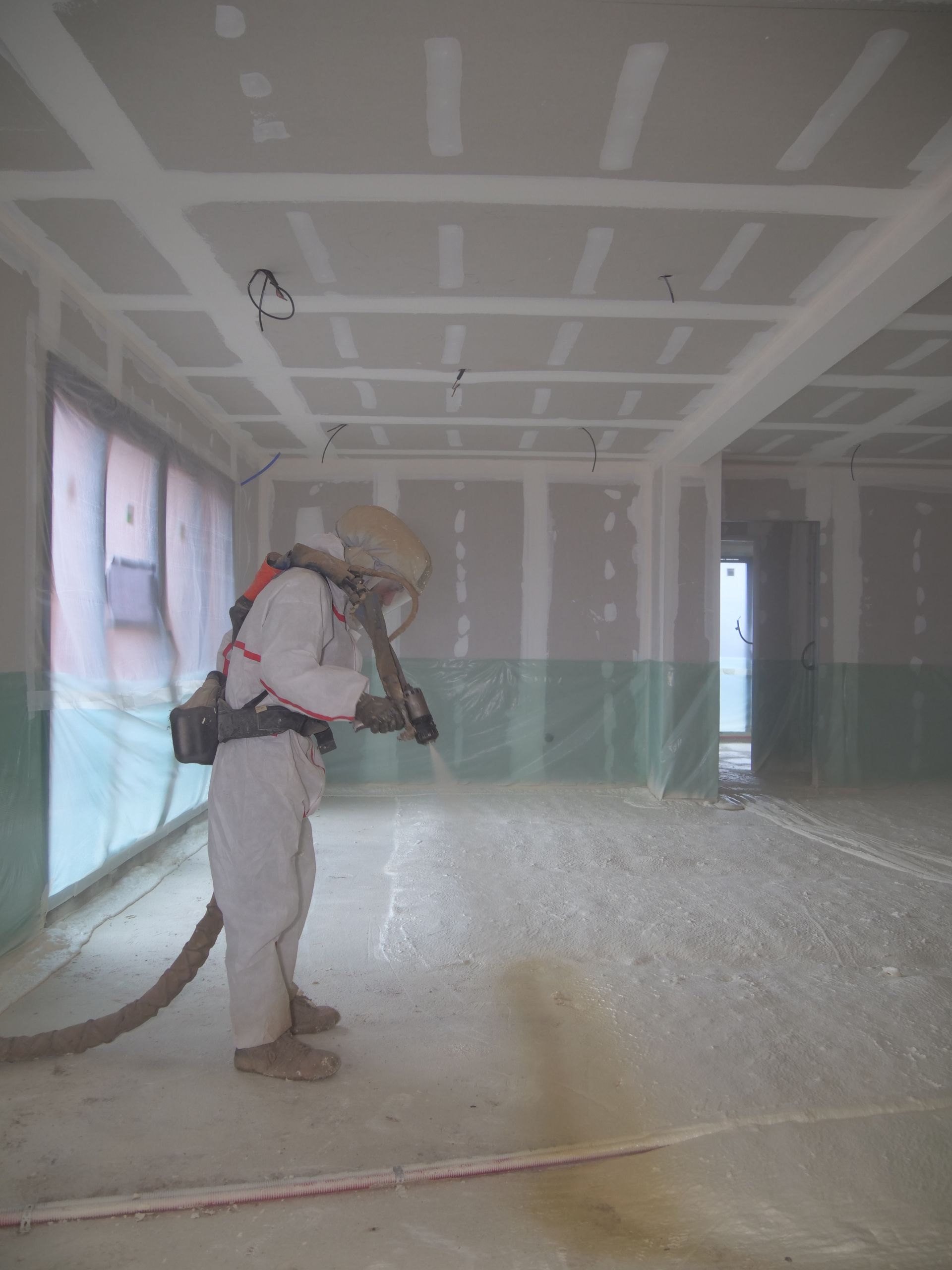 Un homme pulvérise de la mousse sur le sol d'une pièce vide.