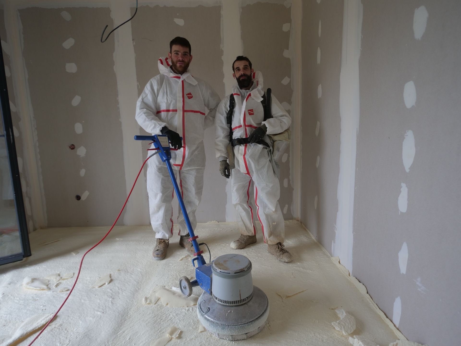 Deux hommes se tiennent l'un à côté de l'autre dans une pièce avec une machine sur le sol.