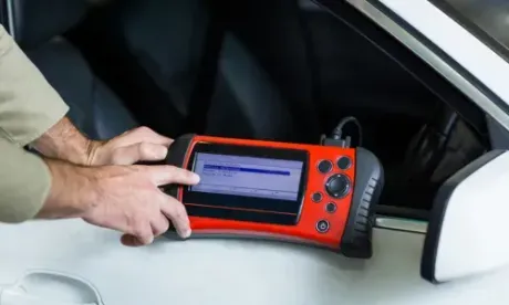 Hands using a red diagnostic tool next to a car's open window, likely checking for issues.