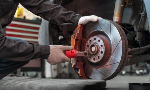 Mechanic working on a car's brake rotor, holding a tool, garage setting.