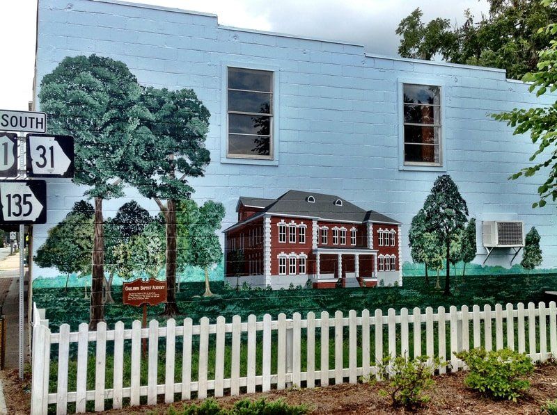 A white picket fence surrounds a mural on the side of a building