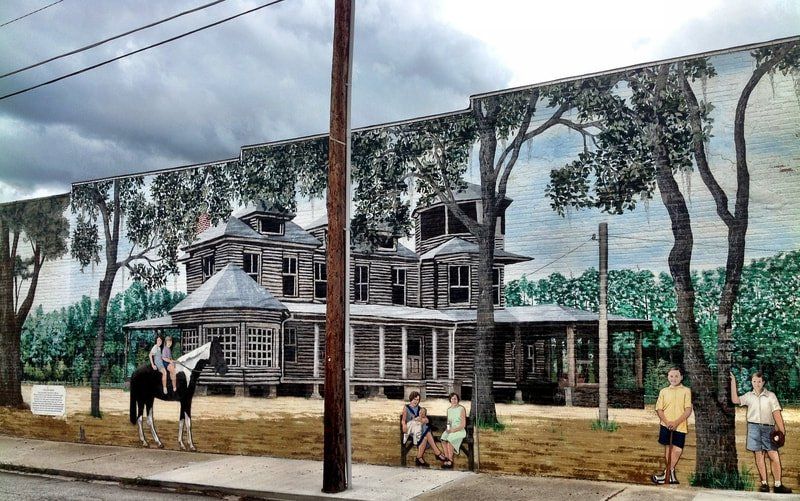 A mural on the side of a building shows people standing in front of a log cabin.