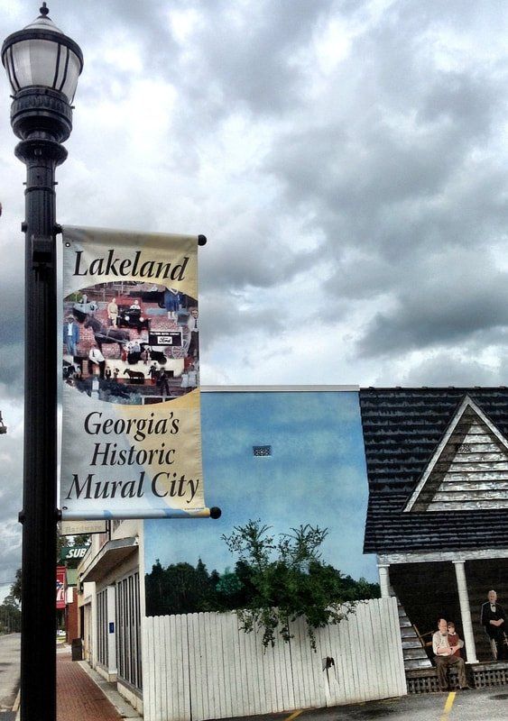 A sign for lakeland georgia 's historic mural city hangs from a street light