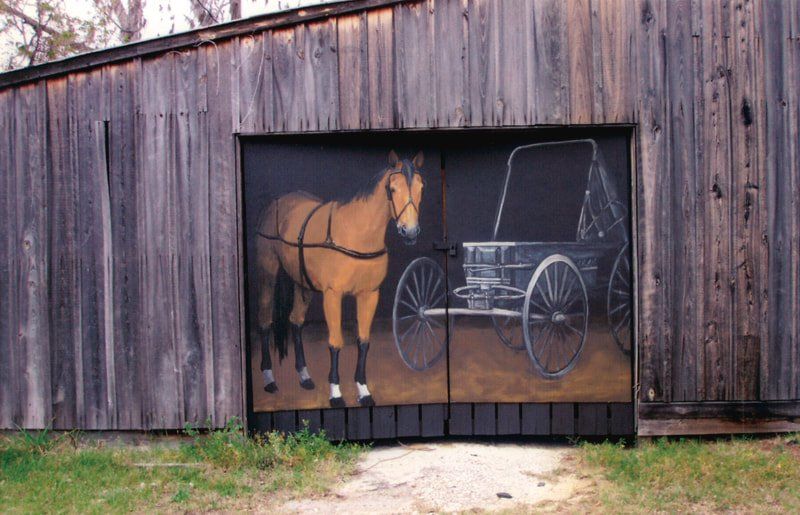 A horse drawn carriage is painted on the side of a barn