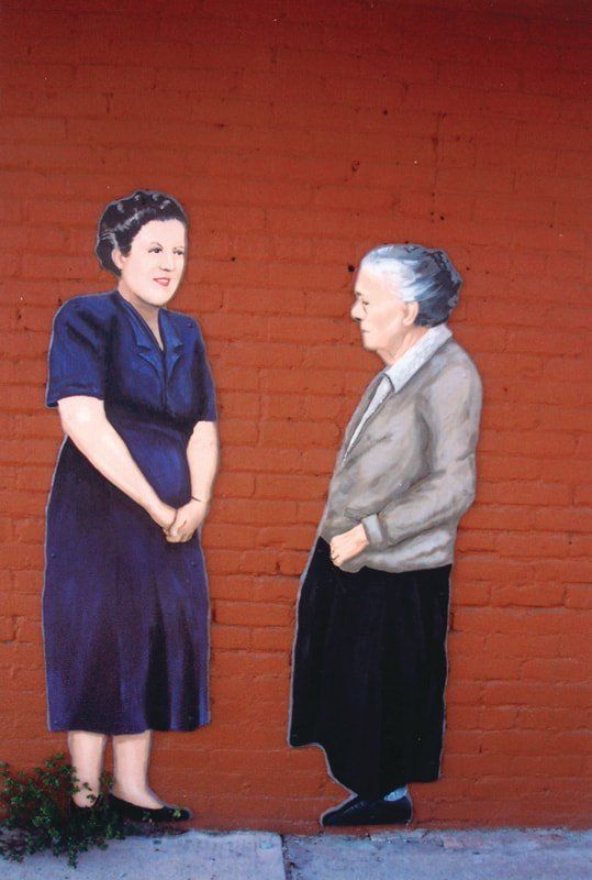 Two women are standing next to each other in front of a red brick wall