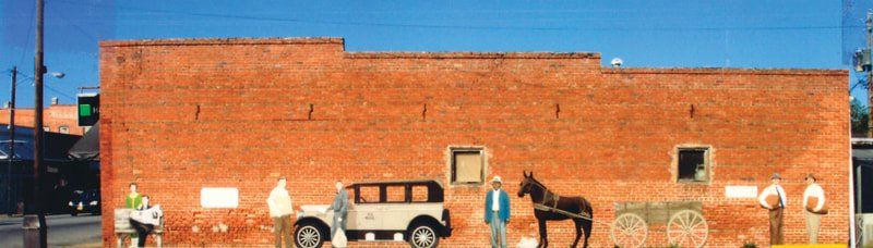 A brick building with a horse drawn carriage and a car parked in front of it.