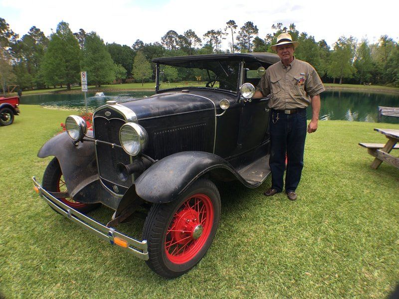 A man is standing next to a black car with red wheels