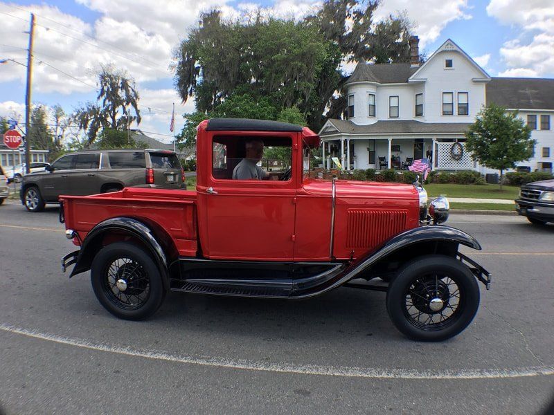 An old red pickup truck is driving down a street