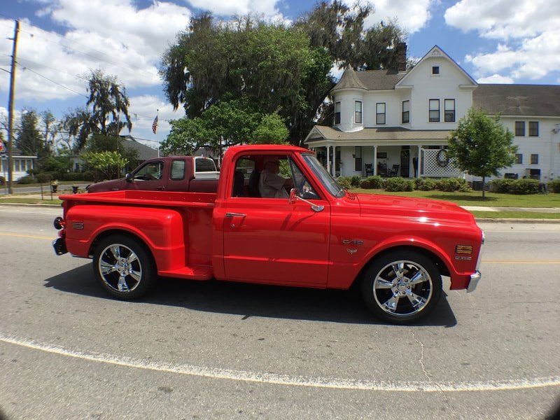 A red truck is driving down a street in front of a white house