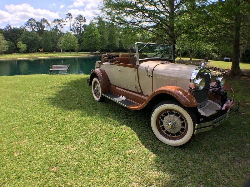 A vintage car is parked in the grass next to a pond.