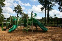 A green playground set in a park with trees in the background.