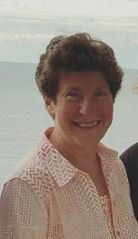 A woman in a pink shirt is smiling in front of the ocean.