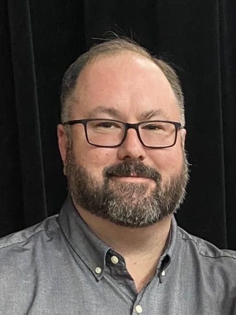 A man wearing glasses and a gray
 shirt.