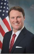 A man in a suit and tie is standing in front of an american flag.