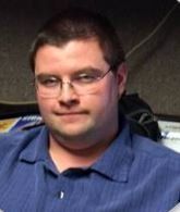 A man wearing glasses and a blue shirt is sitting at a desk.