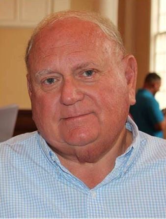 A bald man wearing a blue and white checkered shirt is looking at the camera.