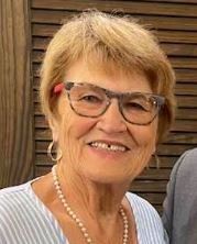 A woman wearing glasses and a pearl necklace is smiling for the camera.