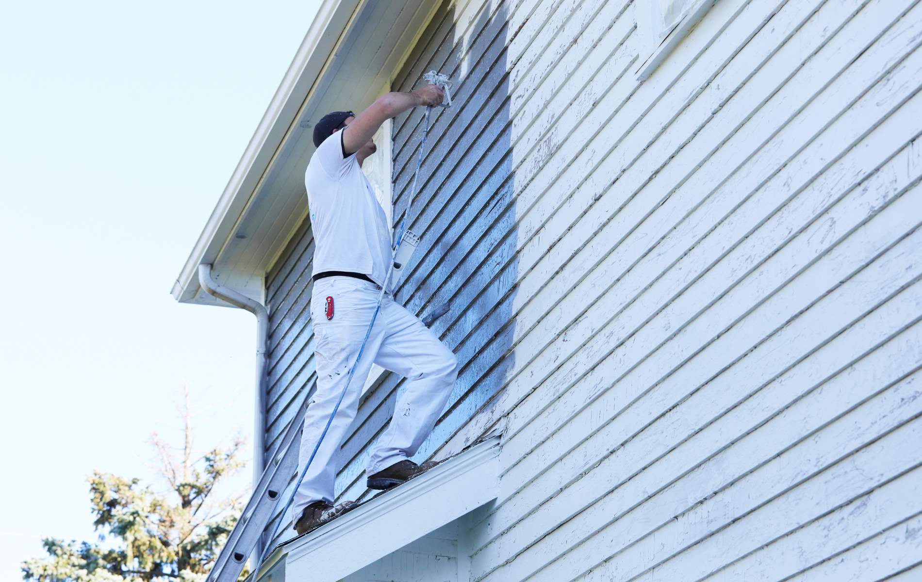 A man is standing on a ladder painting the side of a house.