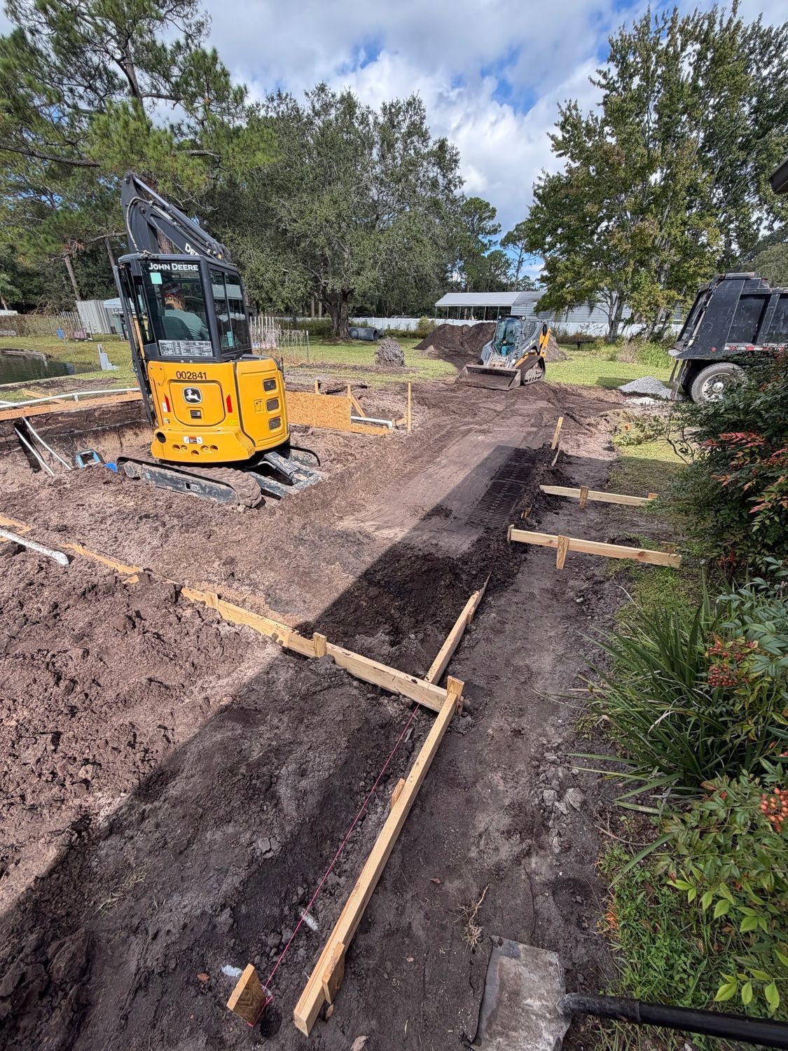 Construction site with yellow excavator, framing, and dirt path.