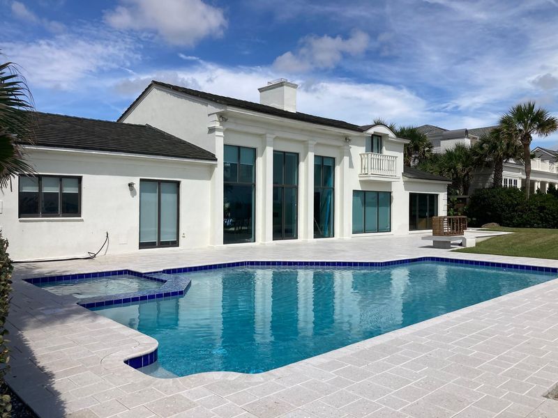 White house with a pool. Blue water, clear sky, and palm trees.