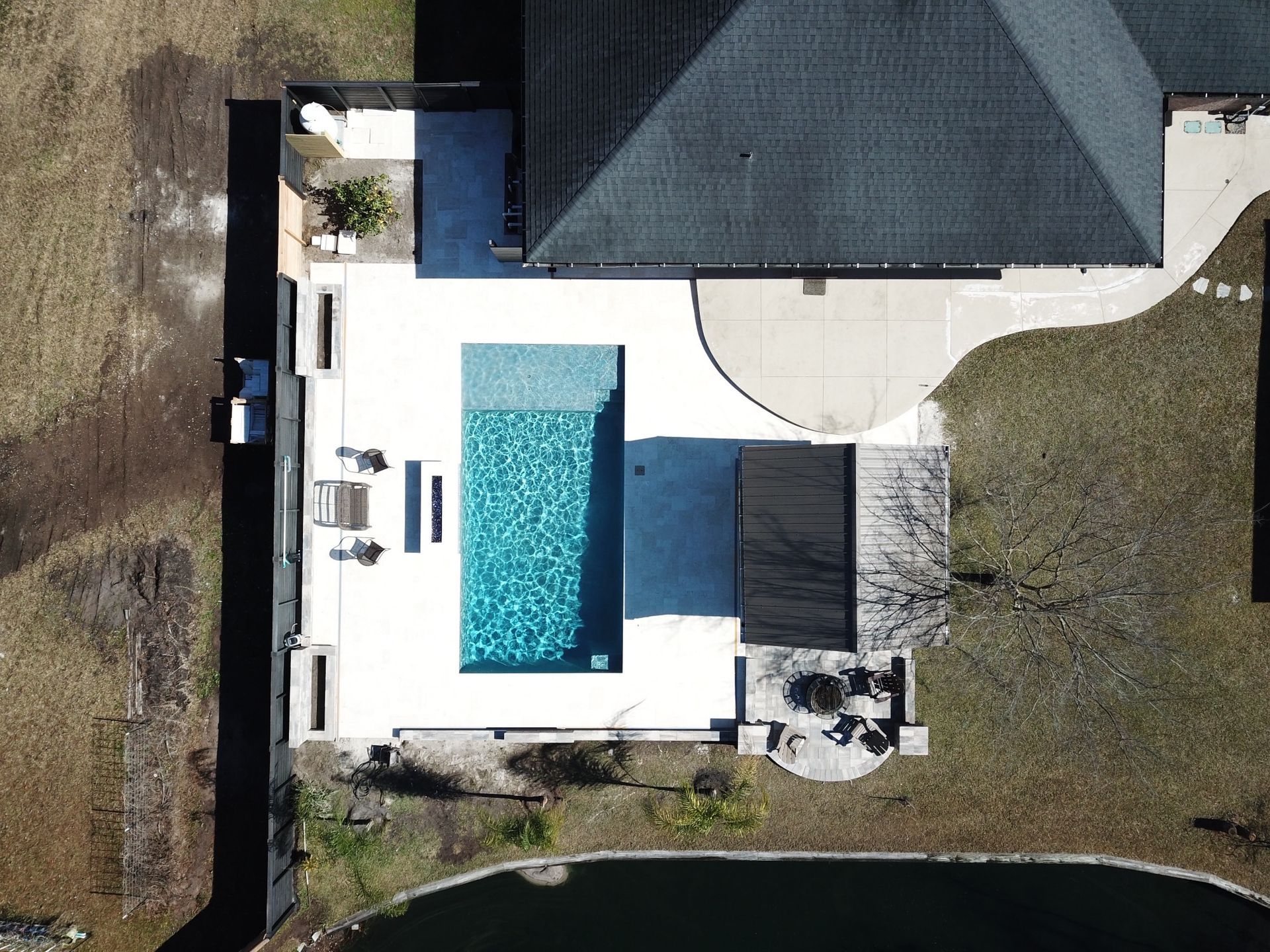 Overhead view of a modern backyard with a rectangular pool, patio, and partially visible house.