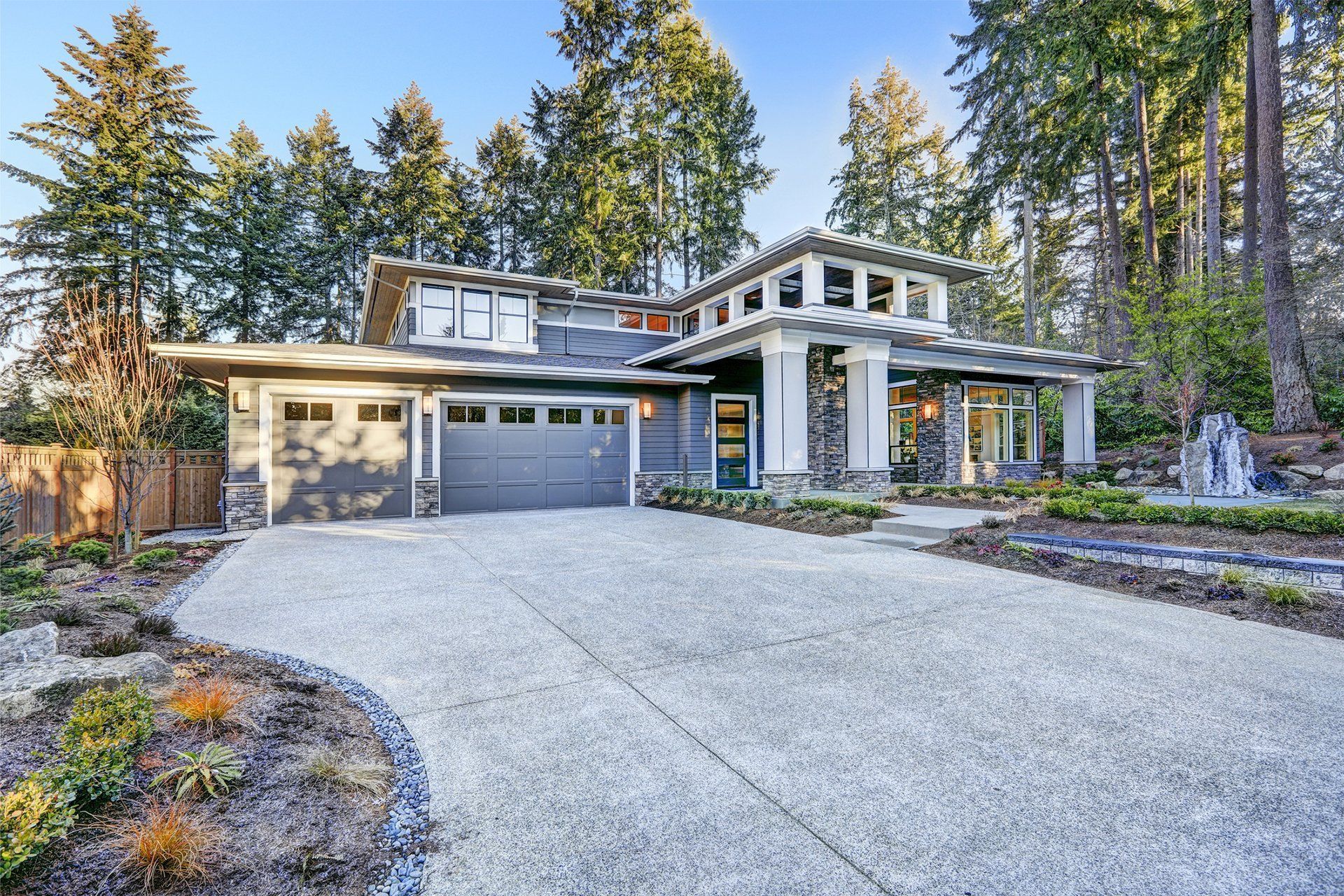 Modern gray house with a concrete driveway, surrounded by trees and landscaping. Modern gray house with a concrete driveway, surrounded by trees and landscaping.