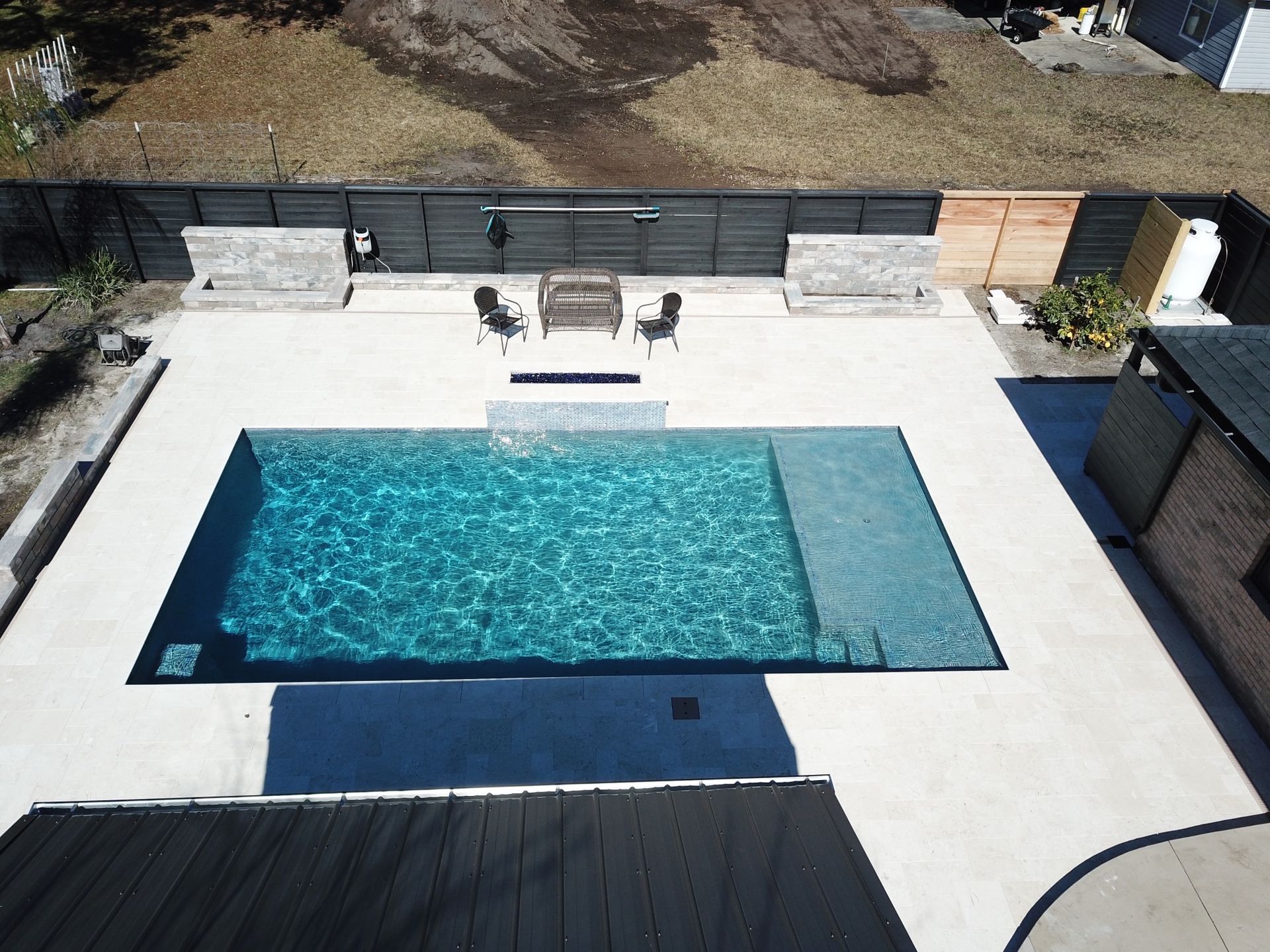 Aerial view of a rectangular pool with turquoise water, surrounded by concrete patio and black fencing.