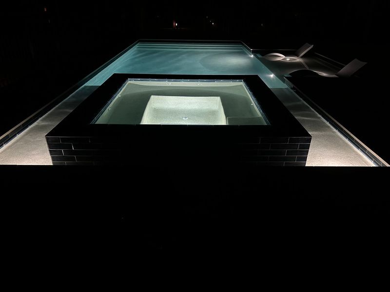 Illuminated swimming pool and hot tub at night.