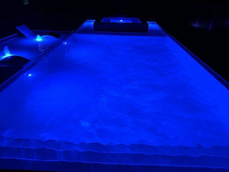 Blue-lit rectangular pool at night. Water surface reflects blue light. Dark surrounding setting.