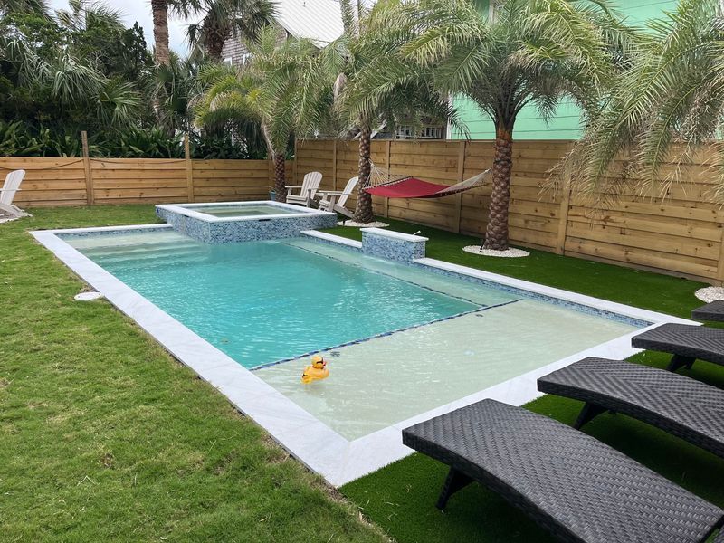 Backyard pool with spa, palm trees, hammock, and lounge chairs.