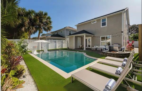 Backyard with pool, lounge chairs, and two-story house, sunny day.