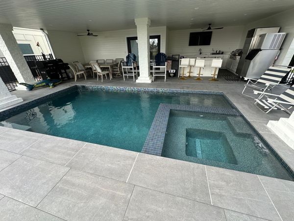 Pool and spa under a covered patio with bar, seating, and appliances.