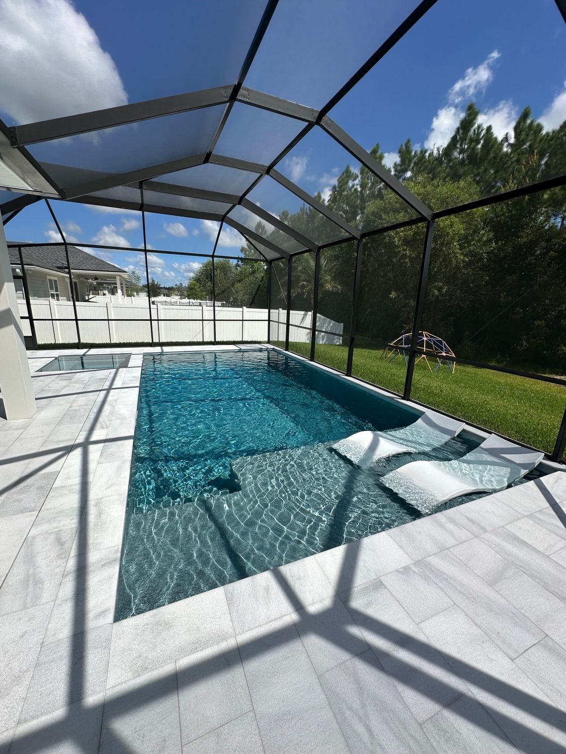 Pool enclosed by a screen. Rectangular pool with blue water and light gray tile surround, under a blue sky.