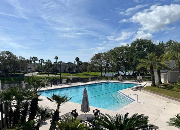 Swimming pool with trees, umbrellas, and blue sky.