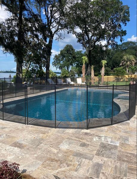 Pool with a black mesh safety fence surrounded by stone pavers, with trees and water in the background.