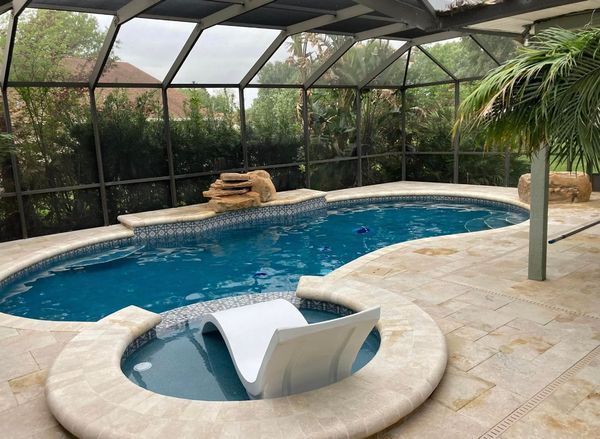 A screened-in backyard pool with stone deck, a waterfall, and a chair in the water.