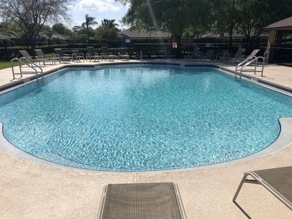 Swimming pool with clear blue water and concrete deck, surrounded by trees and lounge chairs.