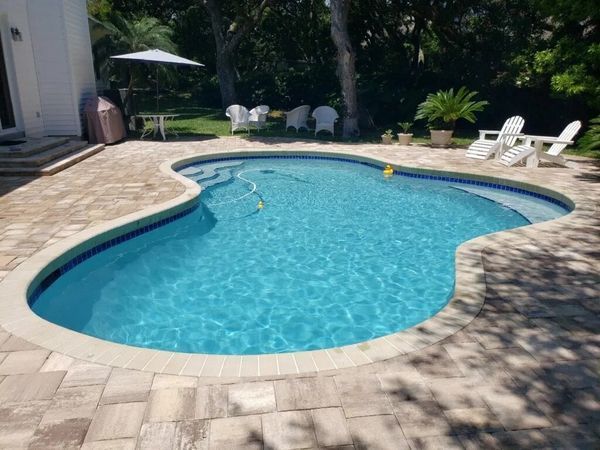 Swimming pool with blue water, surrounded by light-colored paving and white chairs.