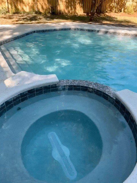 Pool with attached spa, both filled with clear water, blue tile trim, surrounded by concrete.
