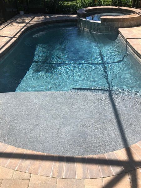 Swimming pool with blue water and gray steps, next to a raised jacuzzi.
