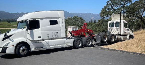 A white semi truck with a tow truck attached to it is parked on the side of the road.