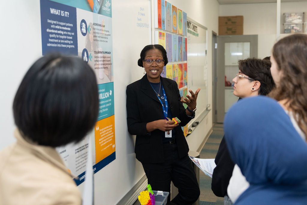 A woman is standing in front of a whiteboard talking to a group of people.