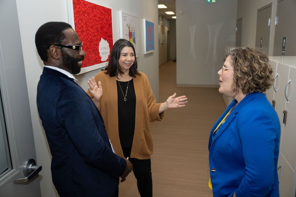 A man and two women are standing in a hallway talking to each other.