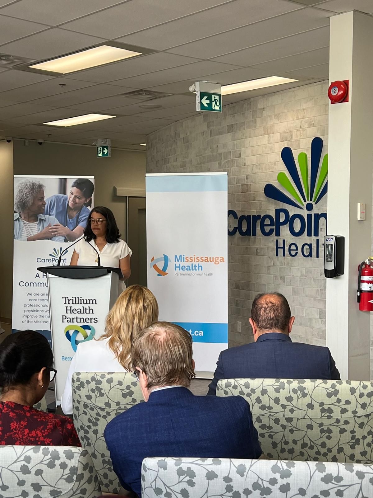 A woman is giving a speech to a group of people in a waiting room.